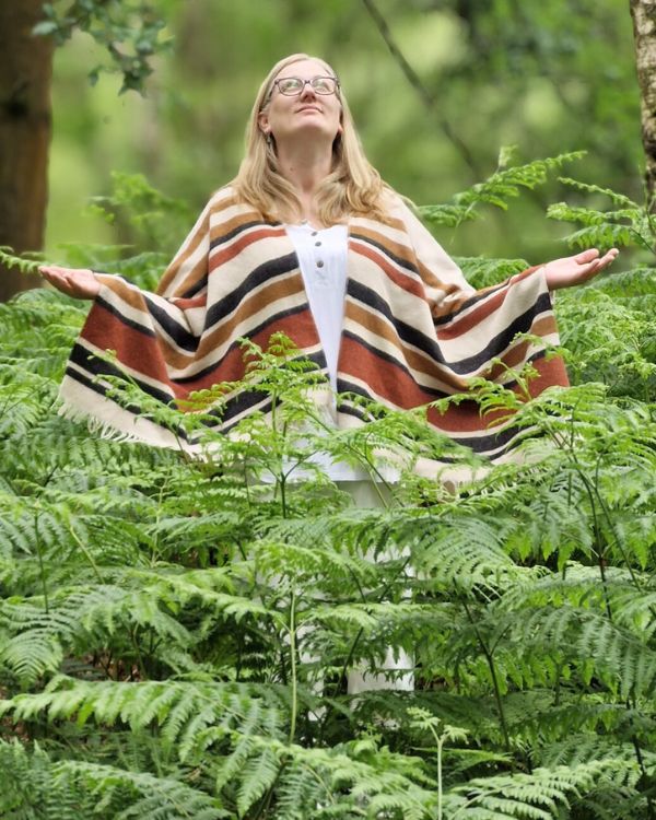 Johanna standing among ferns in a forest with arms open, representing openness, connection and grounded awareness