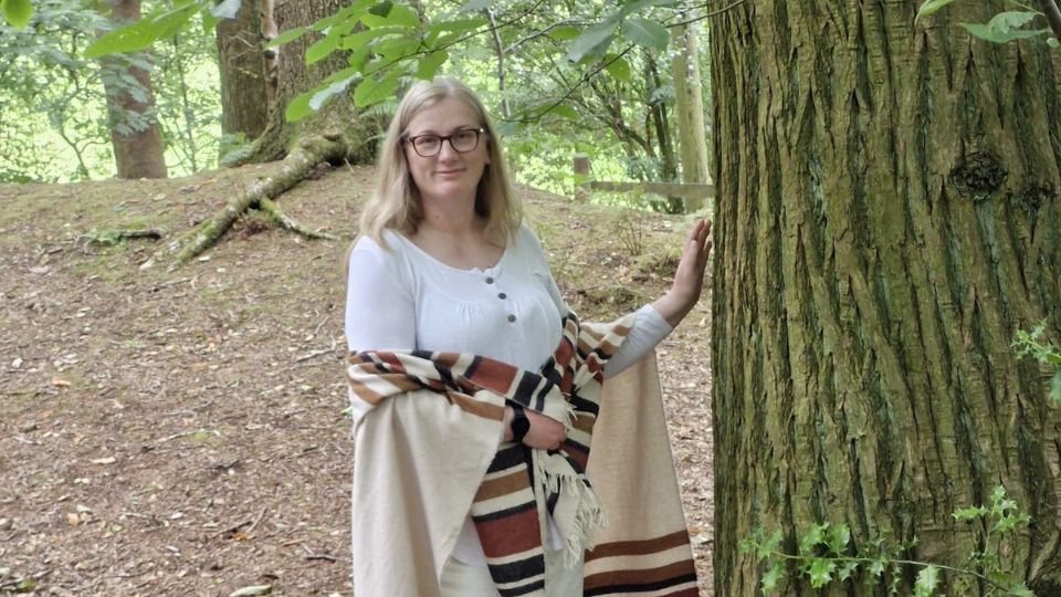 Soie-work-with-me-Soul-Transformation-Therapy Johanna standing in a forest with hand resting on a tree, representing connection with nature and grounded awareness
