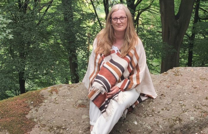 SOIE-practical-wisedom Johanna sitting on a rock in a forest setting, representing calm, presence and connection with nature