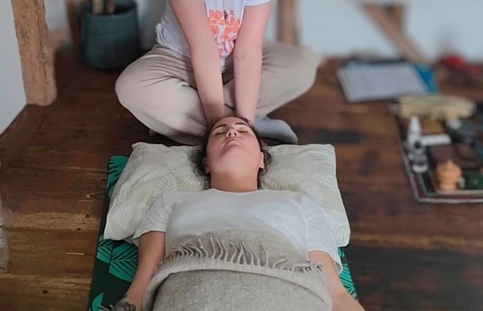 Person lying on a mat receiving hands-on energy healing to the head, representing opening and alignment of the energy field